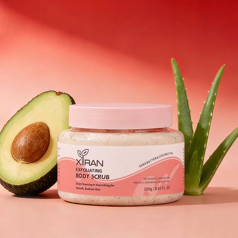Xiran exfoliating body scrub jar with avocado half and aloe plant on a gradient pink background.